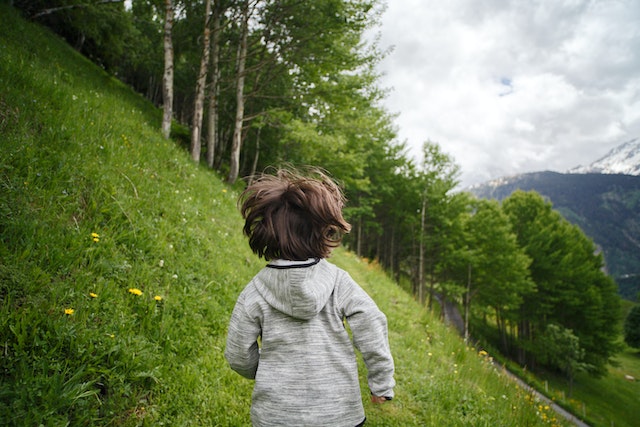 photo of a child running in the green grass field with a sunny sky