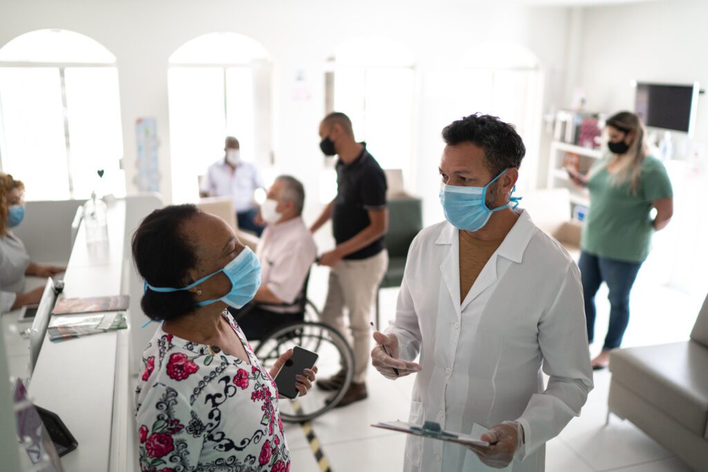Patient arriving at medical clinic and being called by the doctor using face mask - stock photo