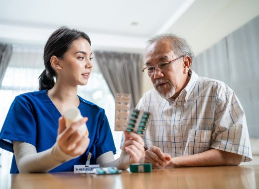 Asian Senior elderly male patient consult with physician nurse at nursing home care. Caregiver therapist pharmacist girl hold medicine pills bottle, explain prescription to older disabled guy in house